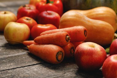 Kabaklar, havuçlar ve kırmızı elmalar ahşap masada.