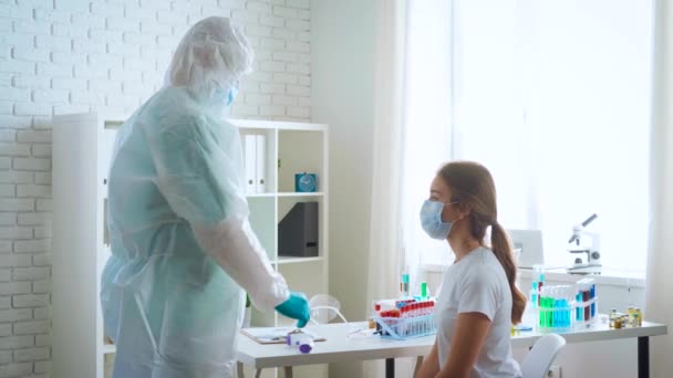 Dokter dalam kostum medis pelindung mengukur suhu pasien wanita dengan termometer inframerah non-kontak di klinik — Stok Video