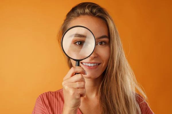 Beautiful young blonde woman looking on you through magnifying glass