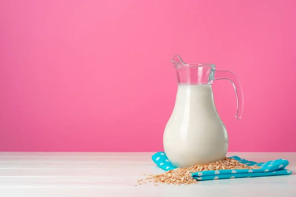 Oat milk in glassware and dry oat flakes on pink background