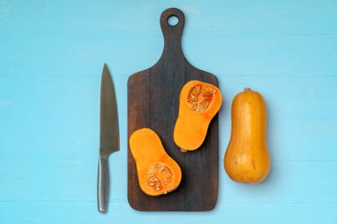 Küçük balkabağı, tahta kesme tahtasında bıçakla ikiye bölünmüş.