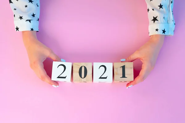 Manos femeninas sosteniendo 2021 Años cubos de madera sobre rosa —  Fotos de Stock