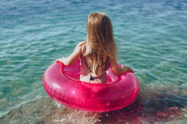 Pembe şişme dairesi olan küçük kız denizde banyo yapıyor.
