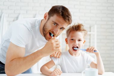 Baba ve küçük oğlu birlikte diş fırçalıyorlar.