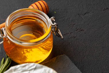 Koyu masada servis edilen peynir parçaları ve bal kavanozu.