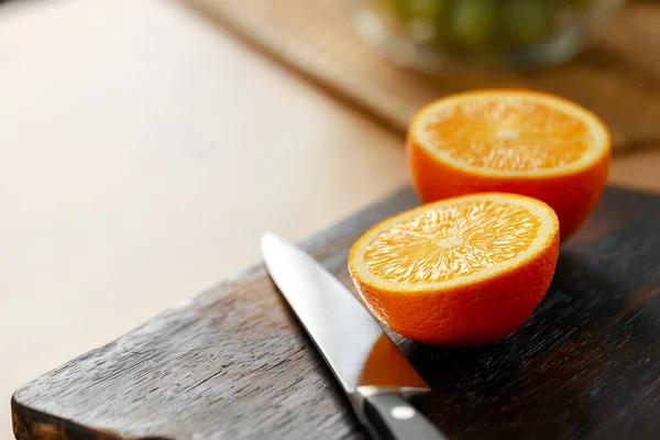 탁자 위에 있는 나무 도마 위에서 오렌지와 칼을 자른다 — 스톡 사진