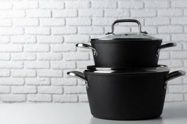 Masadaki siyah mutfak eşyaları beyaz tuğla duvara karşı.