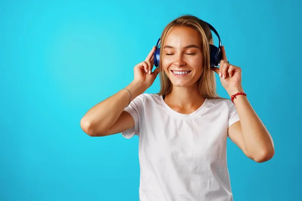 Mujer joven positiva escuchando música con auriculares azules — Foto de Stock
