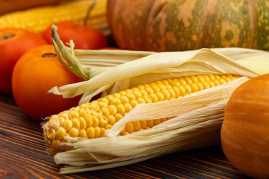 Kahverengi ahşap arka planda balkabağı, mısır ve domates.