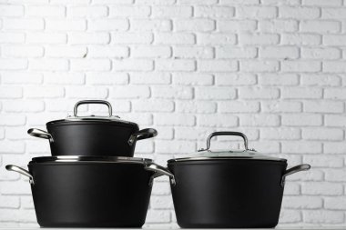 Masadaki siyah mutfak eşyaları beyaz tuğla duvara karşı.