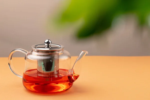 Bulanık yaprakların arka planında siyah çay bulunan cam çaydanlık. — Stok fotoğraf