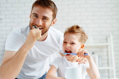Baba ve küçük oğlu birlikte diş fırçalıyorlar.