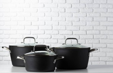 Masadaki siyah mutfak eşyaları beyaz tuğla duvara karşı.