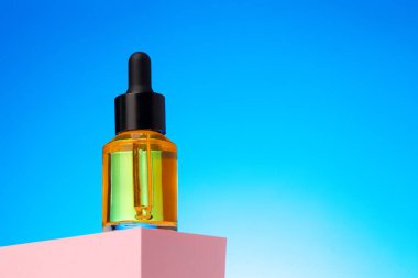 Mavi arka planda pipetli güzellik yağı şişesi.