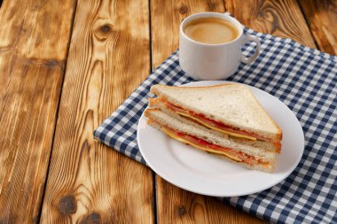 Tahta masadaki peçetede tost sandviçi ve bir fincan kahve.