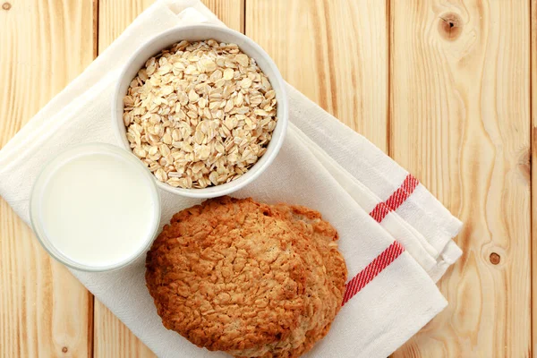 Oat cookies with oat flakes and cup of milk on wooden table — Stock Photo, Image