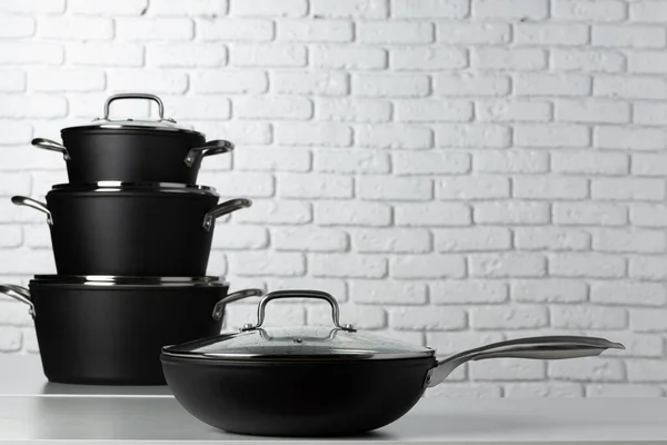 Utensílios de cozinha preto na mesa contra a parede de tijolo branco — Fotografia de Stock