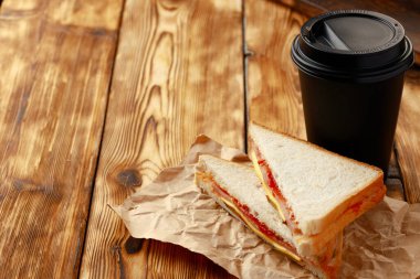 Kağıt üzerinde kızarmış sandviç ve masada bir fincan kahve.