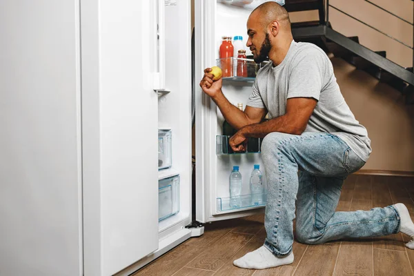 Hombre afroamericano tomando comida de una nevera en su casa — Foto de Stock