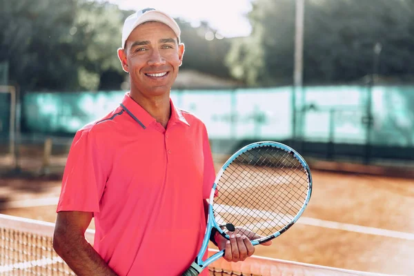 Middle-aged man tennis player with racket standing on court near net