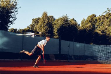 Genç adam sabahları tenis kortunda tenis oynar.