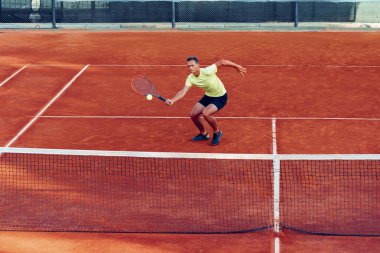 Genç yakışıklı adam tenis kortunda tenis oynuyor.