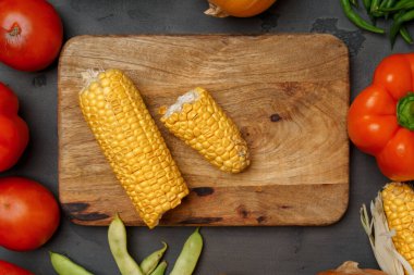 Tahta kesme tahtası ve arka planda dağınık sebzeler.