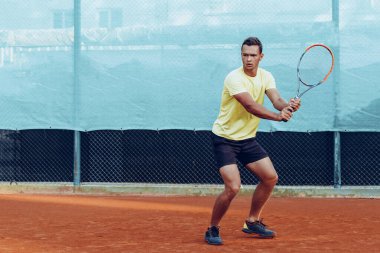 Genç yakışıklı adam tenis kortunda tenis oynuyor.