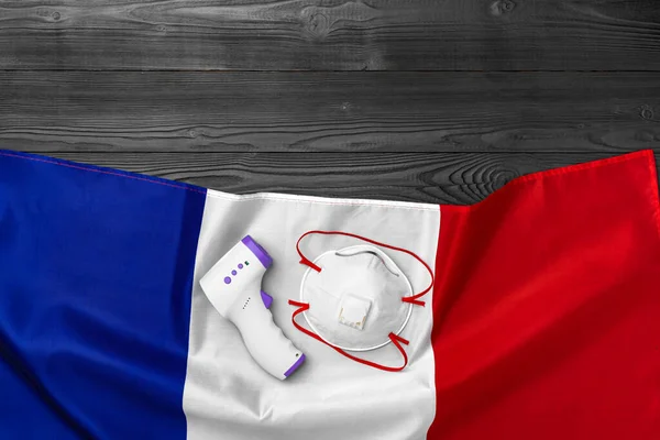 Medizinische Maske und kontaktloses Thermometer auf der Flagge Frankreichs — Stockfoto