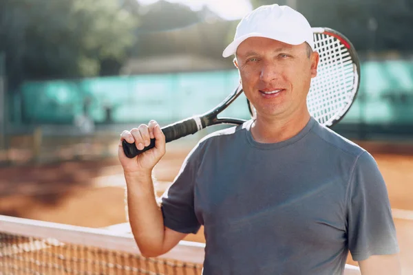 Middle-aged man tennis player with racket standing on court near net