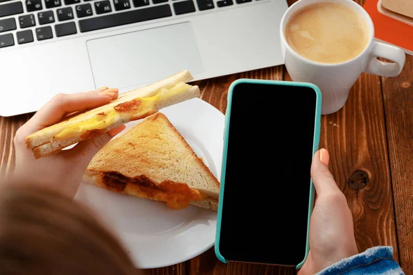 Dłonie kobiety korzystającej ze smartfona podczas przerwy na lunch z kanapką — Zdjęcie stockowe
