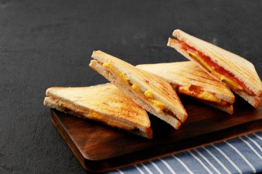 Tahta kesme tahtasında peçeteyle ikiye bölünmüş sandviçler.