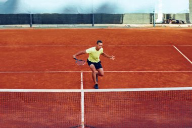 Genç yakışıklı adam tenis kortunda tenis oynuyor.