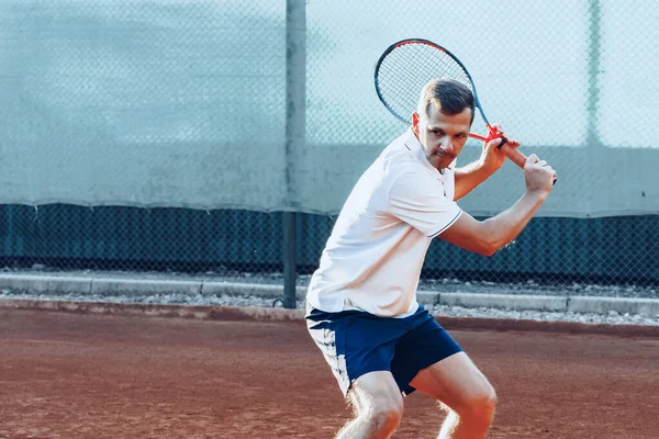 Молодой человек играет в теннис на открытом воздухе на теннисном корте утром — стоковое фото