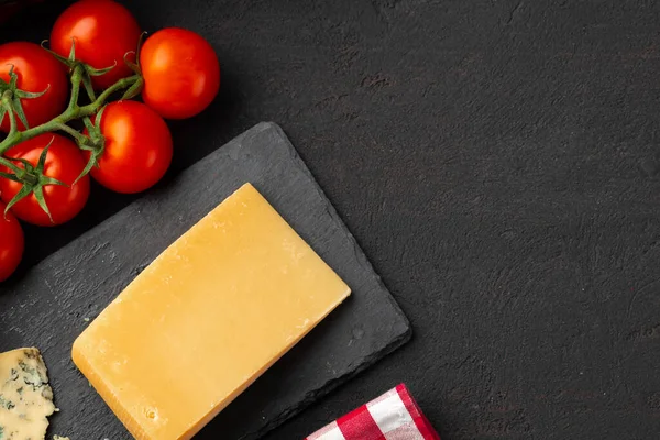 Pomidory wiśniowe i kawałek sera na czarnym stole — Zdjęcie stockowe