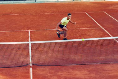 Genç yakışıklı adam tenis kortunda tenis oynuyor.