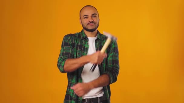 Hombre afroamericano de camisa verde de pie con martillo en las manos sobre fondo amarillo — Vídeos de Stock