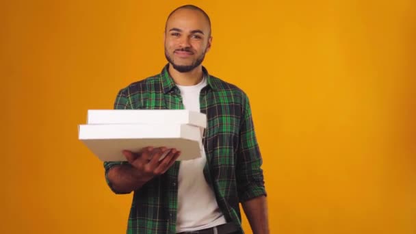 Hombre afroamericano en camisa verde le da dos cajas de pizza dekivery contra abckground amarillo — Vídeos de Stock