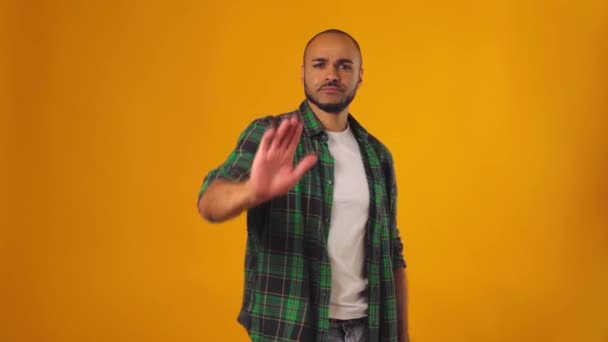 Jeune homme afro-américain en chemise verte montrant stop signe avec sa main sur fond jaune — Video