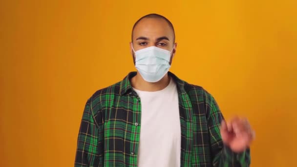 Hombre afroamericano con camisa verde de pie sobre fondo amarillo y quitándose su máscara médica — Vídeos de Stock