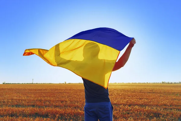 Человек с флагом Украины стоит в поле — стоковое фото
