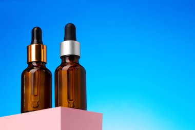 Mavi arka planda pipetli güzellik yağı şişesi.