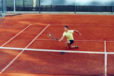 Genç yakışıklı adam tenis kortunda tenis oynuyor.