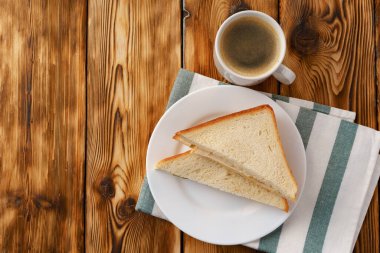 Tahta masadaki peçetede tost sandviçi ve bir fincan kahve.