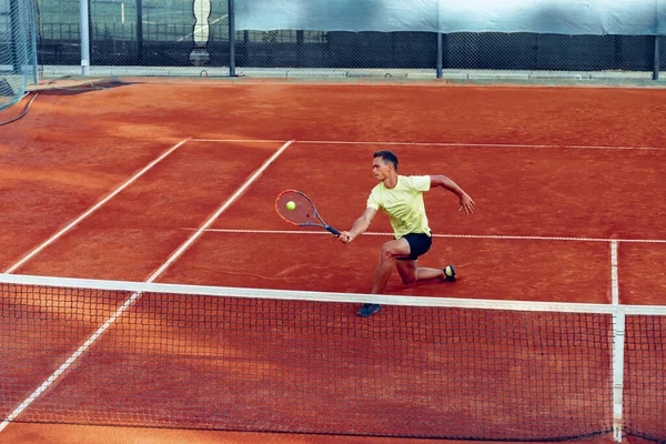 Jovem bonitão jogando tênis na quadra de tênis — Fotografia de Stock