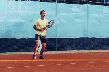 Genç yakışıklı adam tenis kortunda tenis oynuyor.