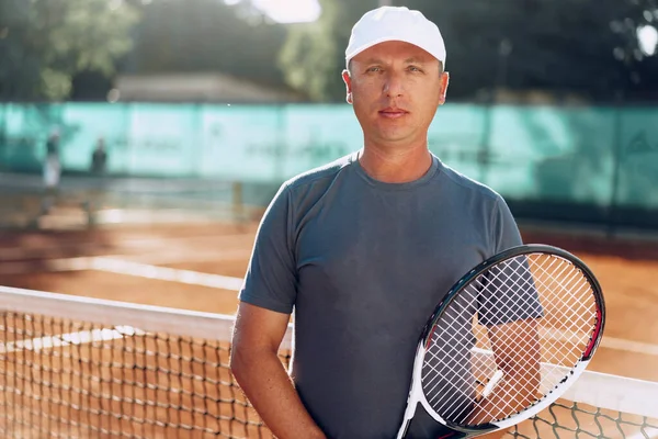 Middle-aged man tennis player with racket standing on court near net