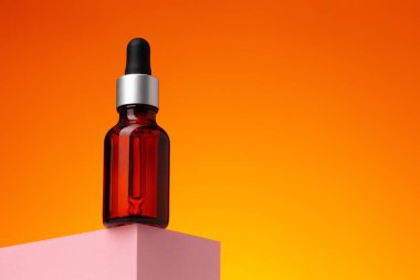 Turuncu arka planda pipetli güzellik yağı şişesi.