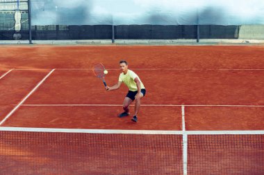 Genç yakışıklı adam tenis kortunda tenis oynuyor.