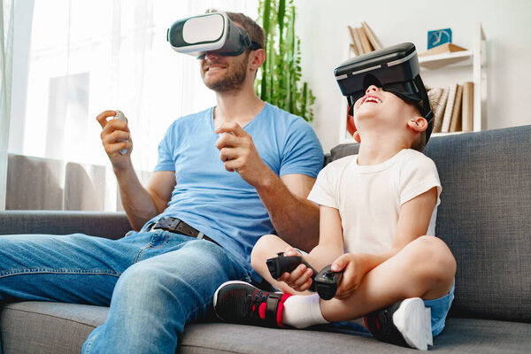 Dad and son sitting on sofa and playing games with VR glasses